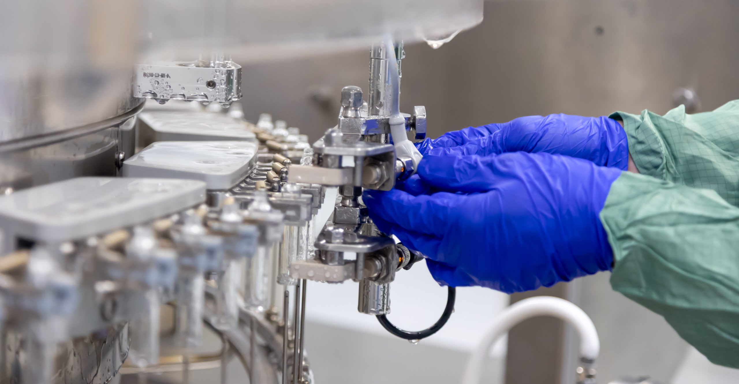 Hands encased in sterile blue gloves meticulously adjusting intricate components of an automated pharmaceutical manufacturing machine within a cleanroom environment. Hands encased in sterile blue gloves meticulously adjusting intricate components of an automated pharmaceutical manufacturing machine