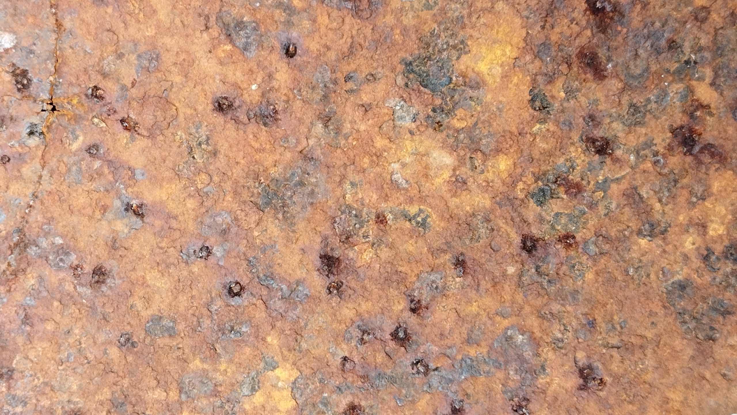 Rusty metal texture with various shades of brown and orange, showing signs of corrosion and oxidation, with small dark spots indicating areas of pitting and decay rusty metal showing pitting corrosion